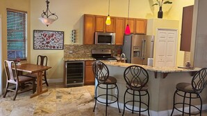 A kitchen with wooden cabinets, a granite countertop, a stainless steel refrigerator, and a bar area with stools. - Casa Palmera: 3 bedroom home (Sebastian)