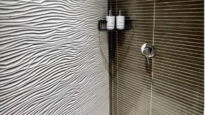 Un baño con pared texturizada, zona de ducha con azulejos oscuros y mampara de vidrio.