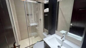 A modern bathroom with a glass-enclosed shower, a white sink, and a large mirror.