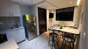 A compact kitchen with a refrigerator, a sink, and a herringbone-patterned backsplash.