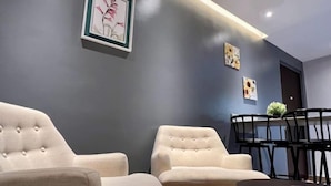 A modern living room with two beige armchairs, a dark grey wall, and a dining area with a black table and chairs.