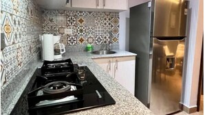 A kitchen with patterned tiles, a stainless steel refrigerator, a gas stove, and a coffee maker.