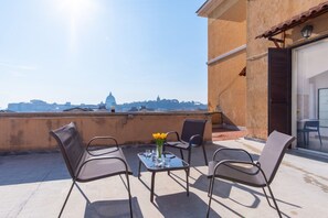 A terrace with a table and chairs, a vase with flowers, and a view of a cityscape. - Elegantis La Dolce Vista Apartment with private terrace and fantastic View (Rome)