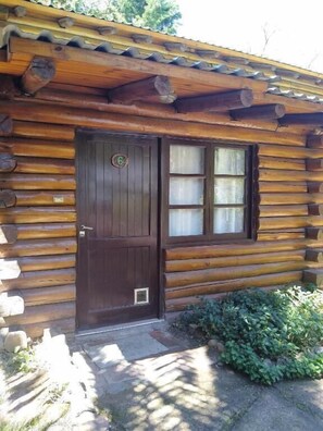 A log cabin with a dark wooden door, a window with frosted glass, and a small porch area with greenery. - Cabañas Pacari Tampu (Las Heras)