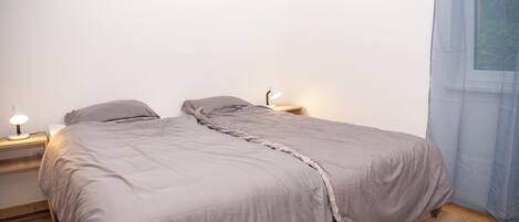 A bedroom with a bed, bedside lamps, and a window with curtains.