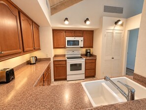 A kitchen with wooden cabinets, a microwave, a stove, a coffee maker, and a sink.