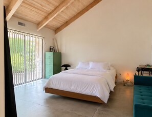 Un dormitorio con una cama grande, un aparador verde, un escritorio con una lámpara y vistas por una ventana.