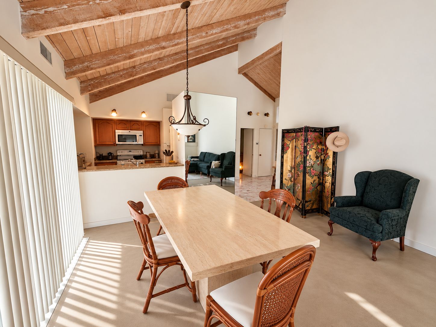 A spacious dining area with a wooden table and chairs, a kitchen in the background, and a traditional room with a decorative screen.