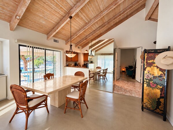 Un comedor amplio con una gran isla, sillas de mimbre y vistas al exterior mediante puertas correderas.