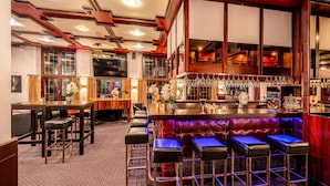 Uma área de bar com balcão de madeira, vários bancos e um espaço de estar com bancos acolchoados.