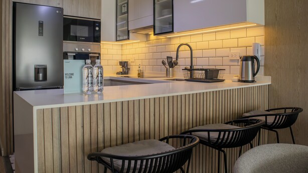 Une cuisine moderne équipée d’un réfrigérateur en acier inoxydable, d’un four à micro-ondes, d’un évier et d’une machine à café. On y trouve également deux tabourets de bar et un mur recouvert de panneaux en bois.