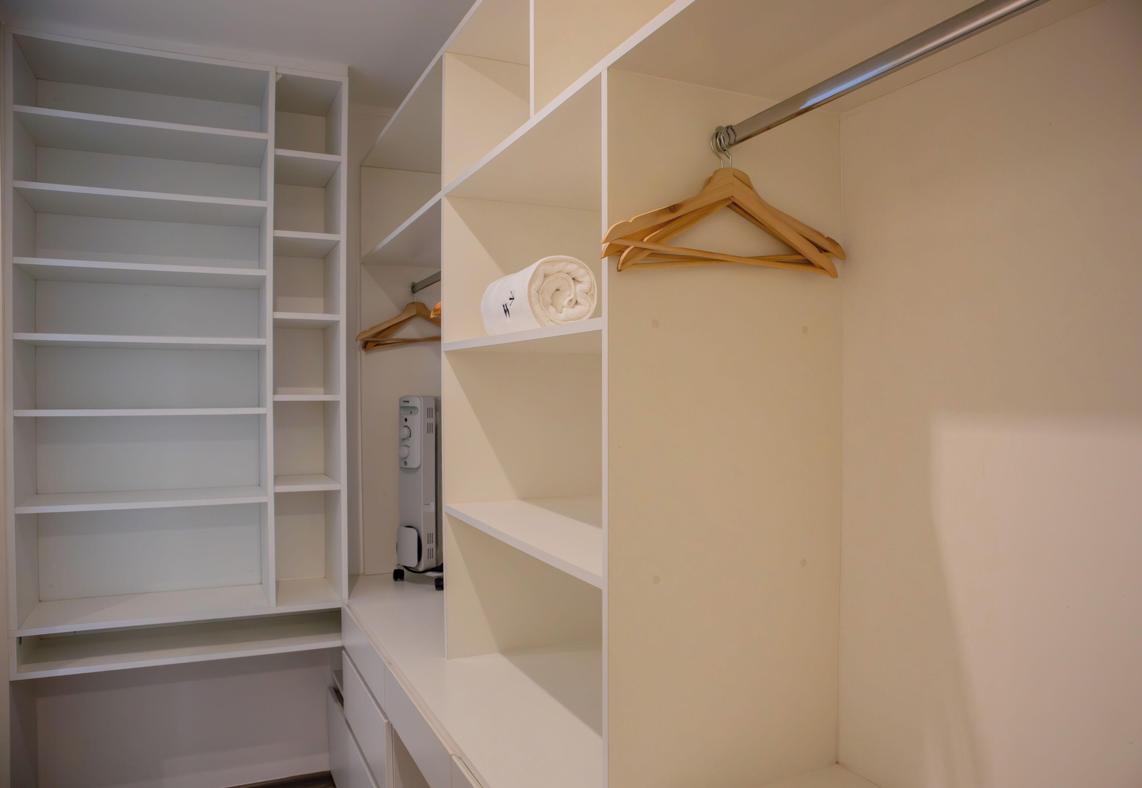 Un dressing avec de nombreuses étagères et un espace pour suspendre les vêtements, un appareil électroménager blanc et des cintres en bois.