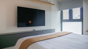 Une chambre d’hôtel moderne dotée d’un grand lit, d’un téléviseur à écran plat fixé au mur et d’une fenêtre avec des stores.