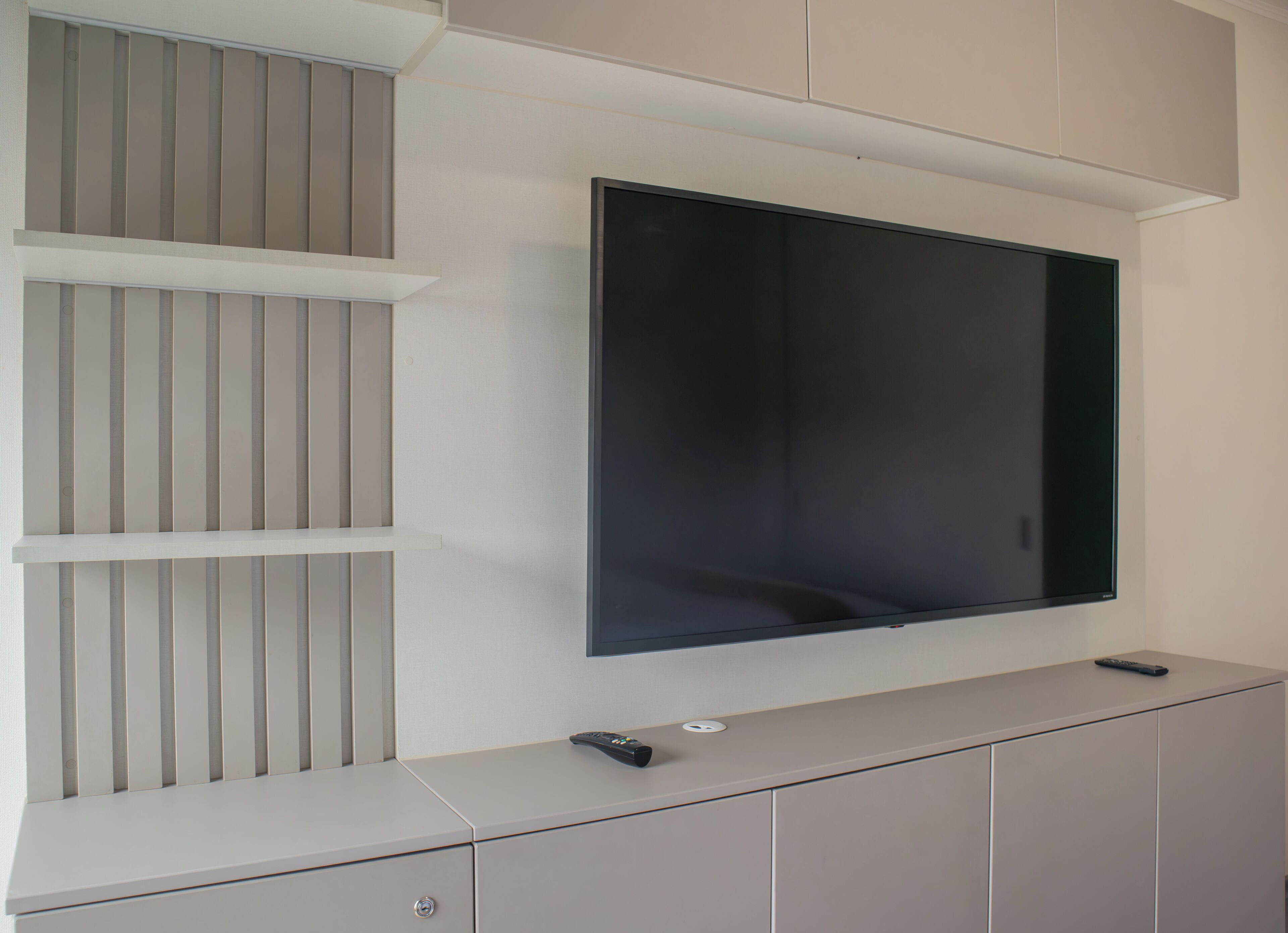 Een flatscreen televisie hangt aan de muur, met een minimalistische wandplank eronder.