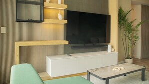 Un salon moderne avec un téléviseur à écran plat fixé à un mur en bois, une console blanche, un canapé vert et une table basse.