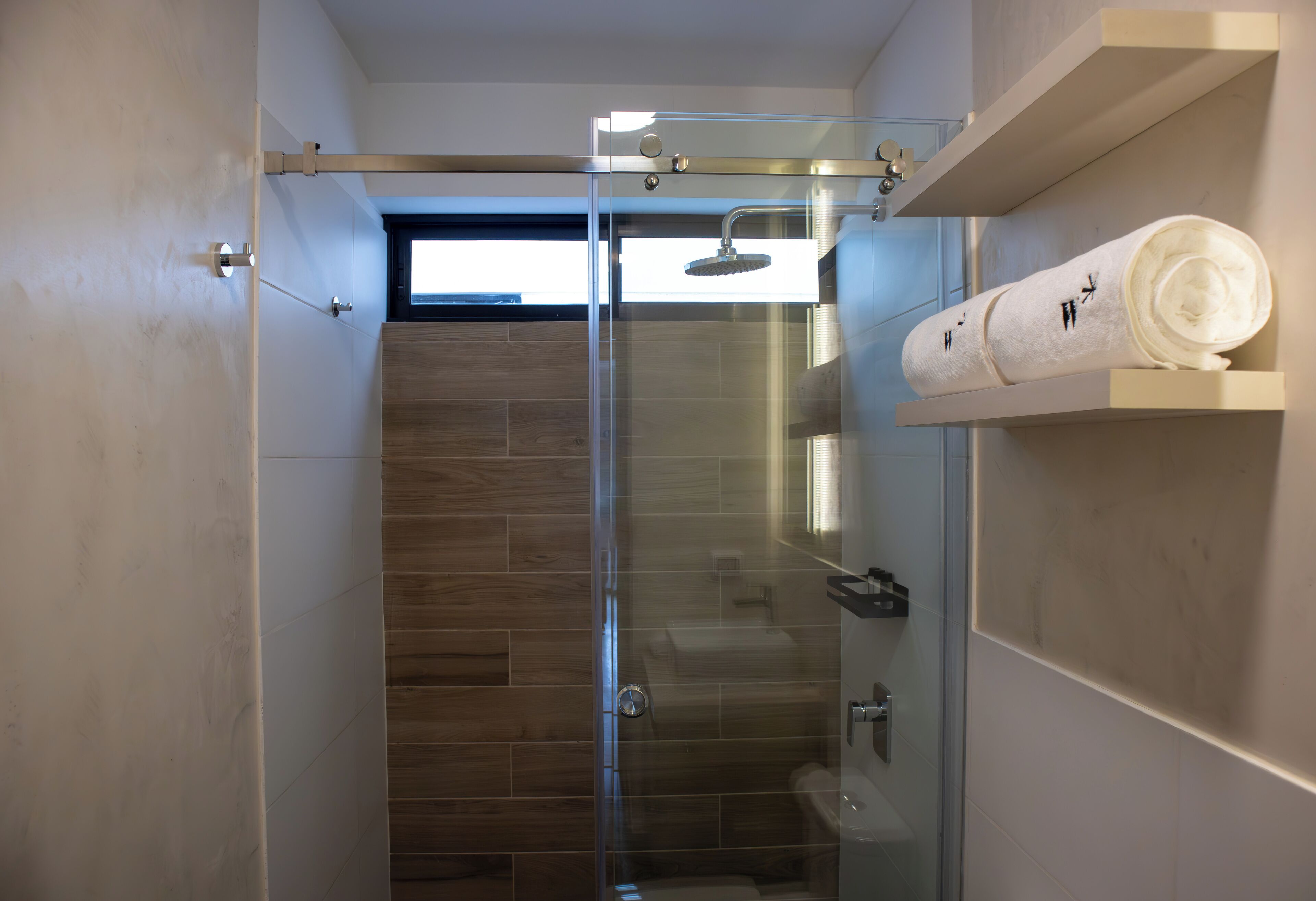 Ein modernes Badezimmer mit Duschkabine aus Glas, Duschbereich mit Holzboden und Handtuchhalter mit Handtüchern.