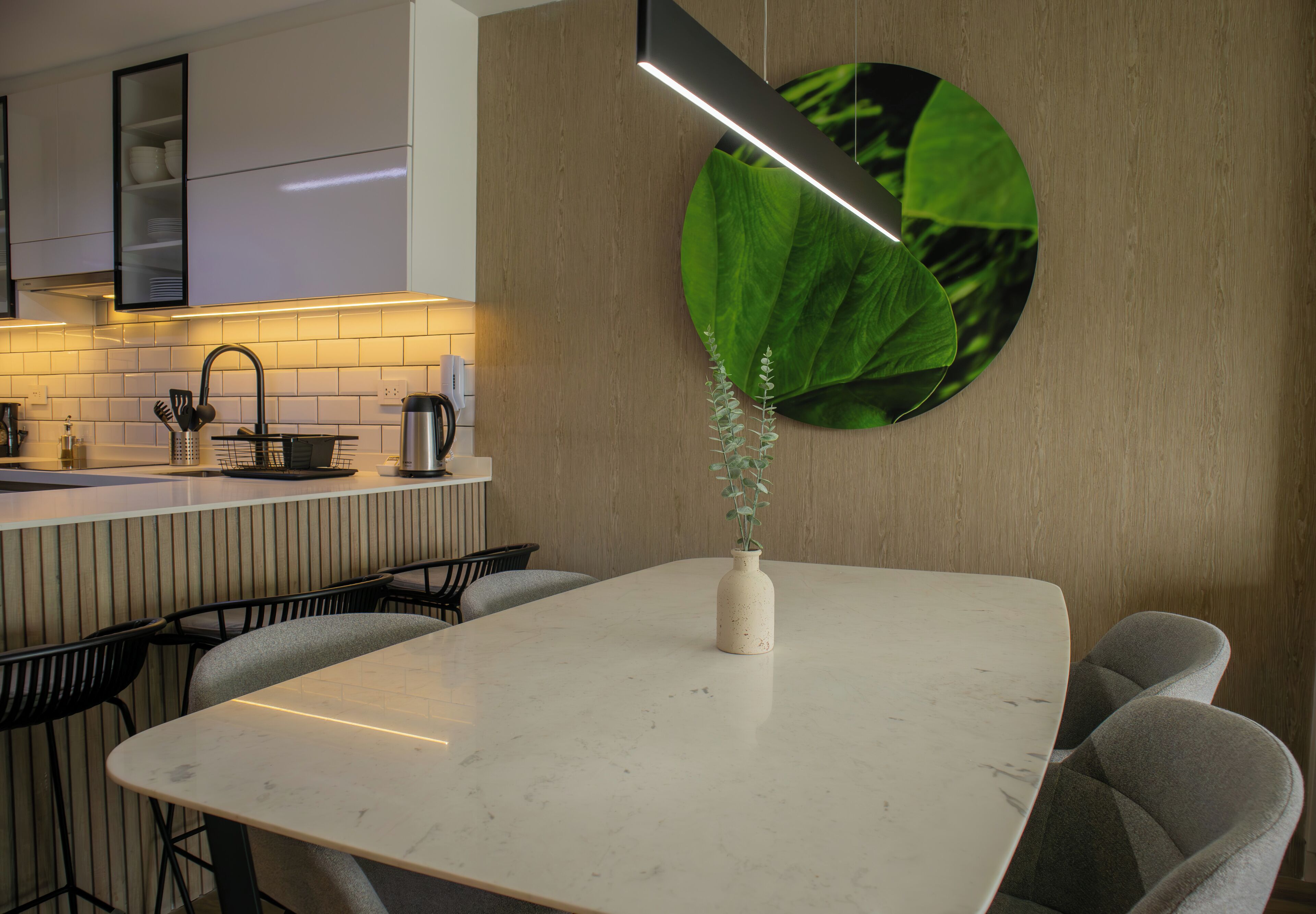 Een moderne keuken met een witte marmeren aanrecht, zwarte stoelen en een groot kunstwerk van een groene blad.