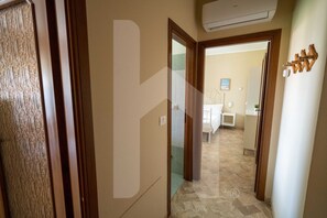 Un pasillo de hotel con una puerta de madera, un mamparo de cristal y un baño a la vista al fondo.