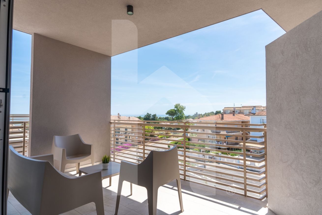 Un balcón con dos sillas y una mesa, con vista a una zona residencial con edificios escalonados y cielo despejado.