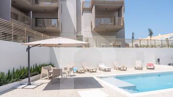Area piscina moderna con lettini e una vasca, circondata da un edificio bianco con balconi.