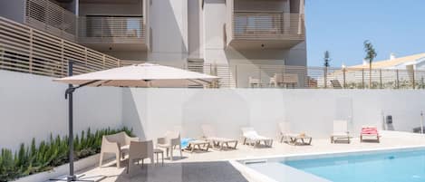 A modern pool area with lounge chairs and a pool, surrounded by a white building with balconies.