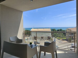 Un balcó amb dues cadires i una taula petita, amb vista a una zona residencial i al mar.