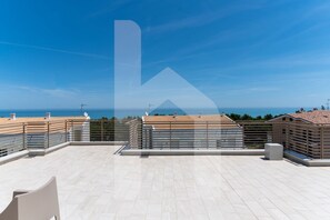 A rooftop terrace with a clear view of the sea, a tiled floor, and a railing.