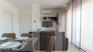 A modern living room with a sofa, a dining table set for two, and a TV mounted on the wall. - Holiday home ELEA is the 2025 novelty that will give you a holiday in Pineto but with the charm of a new modern construction, fresh and designed with all the comforts. he Clio apartment has a large living room with kitchenette and sofa bed at the entranc (Pineto)