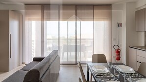 A modern living room with a sofa, a dining table set for two, and a sliding glass door leading to a balcony. - Holiday home ELEA is the 2025 novelty that will give you a holiday in Pineto but with the charm of a new modern construction, fresh and designed with all the comforts. he Clio apartment has a large living room with kitchenette and sofa bed at the entranc (Pineto)
