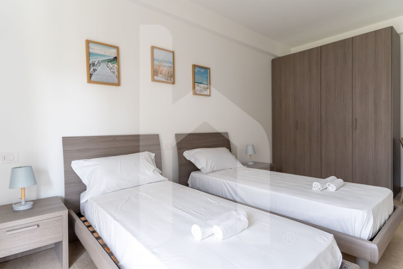 A hotel room with two single beds, a wooden wardrobe, and a nightstand with a lamp.