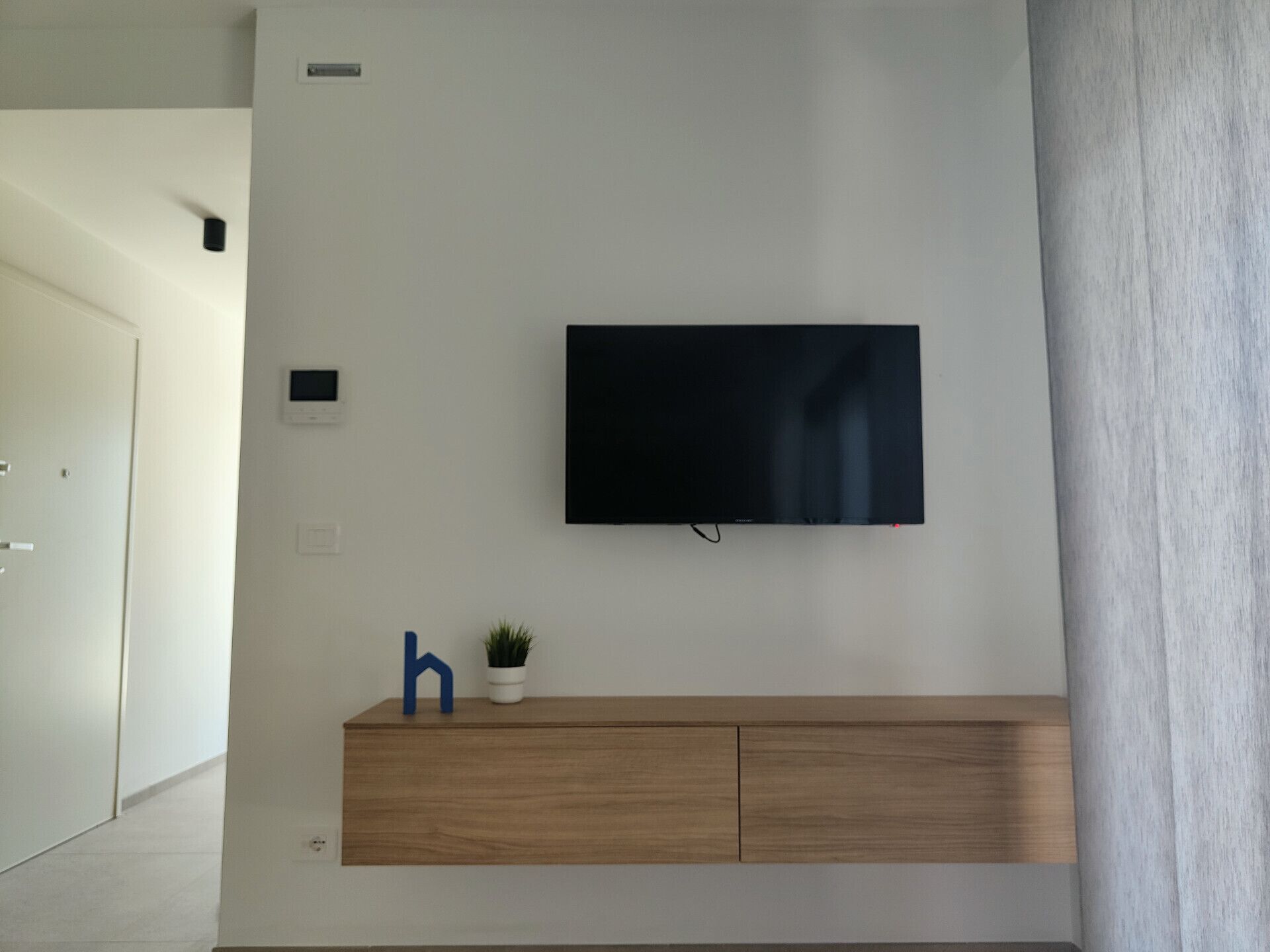 A modern living room with a mounted flat-screen TV, a wooden cabinet, and a small potted plant.