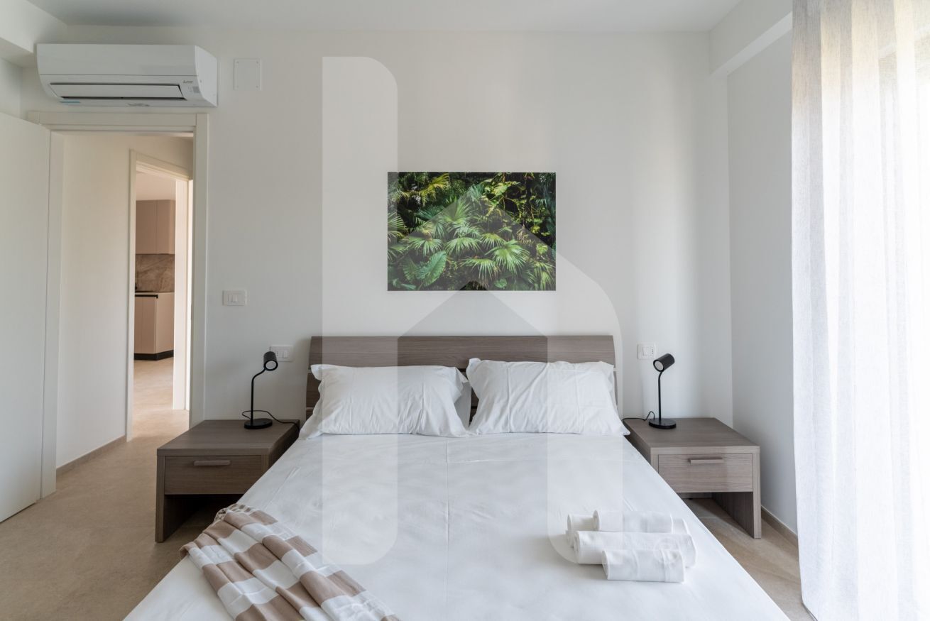A modern bedroom with a large bed, two bedside tables, an air conditioning unit, and a forest-themed wall art.