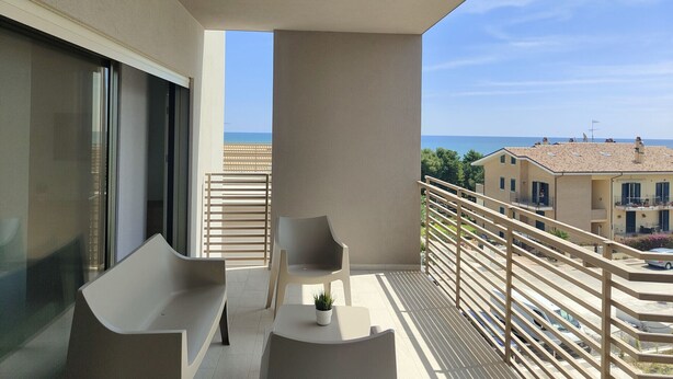 Een balkon met een bank, twee stoelen, een bijzettafeltje en een bloempot.
