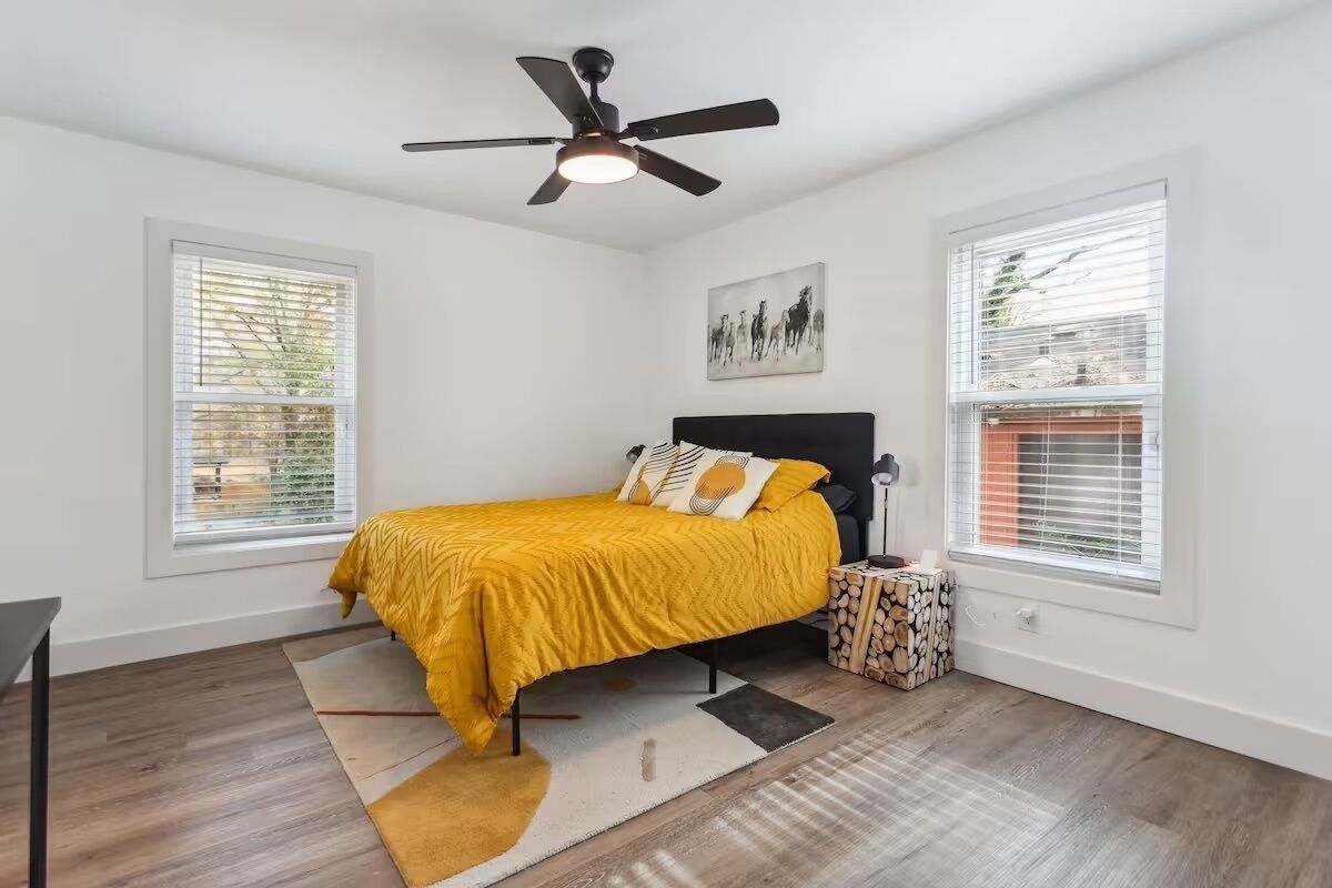 Une chambre à coucher avec un lit, un ventilateur de plafond, une fenêtre et une petite table de chevet sur laquelle se trouve une bougie.