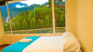 A hotel room with a bed, a blue and white bedspread, a white pillow, and a remote control on a small table.