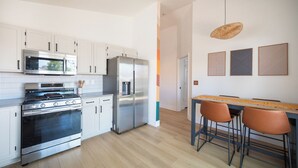 Una cocina moderna con electrodomésticos de acero inoxidable, armarios blancos y piso de madera. Hay dos taburetes de bar y un colgante.