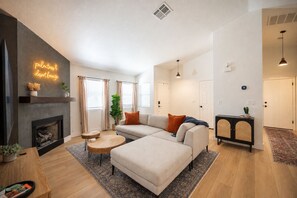 A modern living room with a fireplace, a sofa, a coffee table, and a dining area with a black cabinet.
