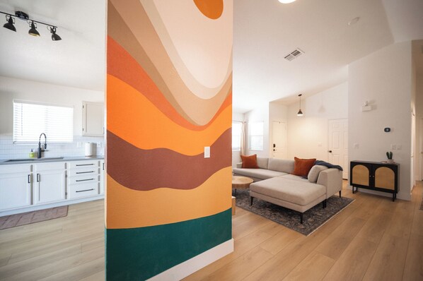 Un appartement moderne comprenant une cuisine, un espace de vie et un grand mur décoré d’une œuvre abstraite.