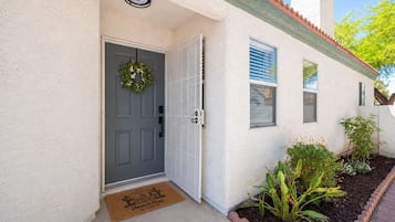 A house with a grey door, a doormat, and a small garden with plants and a brick border.