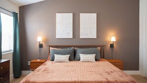 Un dormitorio con una cama grande, dos mesitas de noche, dos lámparas de pared y dos cuadros enmarcados en la pared.