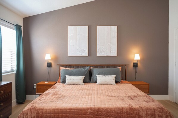 Ein Schlafzimmer mit einem großen Bett, zwei Nachttischen, zwei Wandlampen und zwei gerahmten Bildern an der Wand.