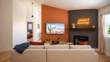 Una sala de estar con un sofá seccional grande, un televisor de pantalla plana en la pared, una chimenea y un letrero de neón.