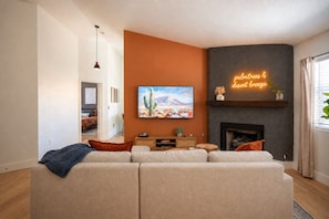 Una sala de estar con un sofá seccional grande, un televisor de pantalla plana en la pared, una chimenea y un letrero de neón.