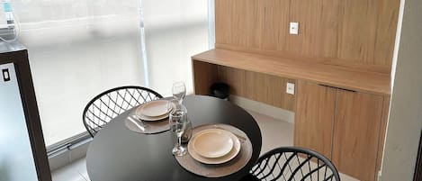 Uma área de refeições moderna com mesa redonda, cadeiras pretas e iluminação pendente.