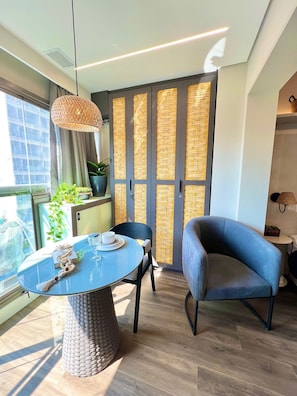 A modern room with a round table, a blue chair, a hanging light fixture, and a large window with a view.