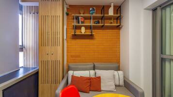 A compact living space with a sofa set, a wooden partition, and a small bookshelf against a brick wall.