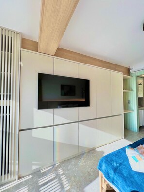 A modern room with a flat-screen TV mounted on a wall, a wooden ceiling beam, and a tiled floor.