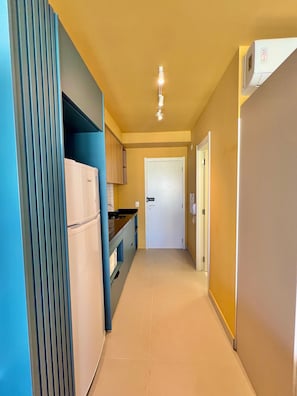 Un couloir étroit avec un coin cuisine sur la gauche, une porte au fond et un appareil de climatisation sur la droite.
