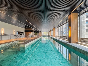 A modern indoor swimming pool with a unique ceiling design, large windows, and a clear view of the outside. - Innvista - AirBrooklin (São Paulo)