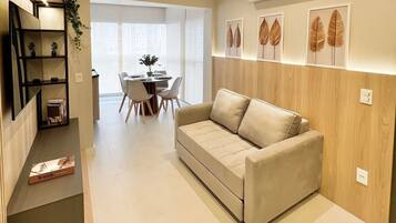 A modern living room with a sofa, a dining area with a table and chairs, and a hallway with a staircase.